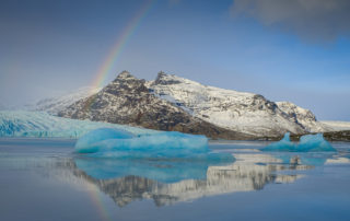 icebergs and mountains around lagoon with rainbow in Iceland